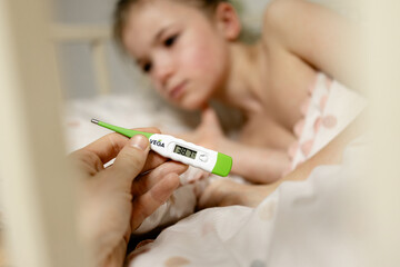 a photo of an electronic thermometer in the hands of a parent measuring the body temperature of their child, fever in a sick child