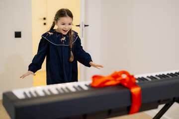 A young girl excitedly opens a gift-wrapped keyboard with a red ribbon.