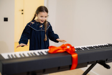 A young girl excitedly opens a gift-wrapped electronic keyboard with a red ribbon.