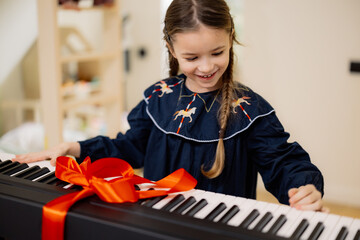 A young girl excitedly opens a gift-wrapped electronic keyboard with a red ribbon.