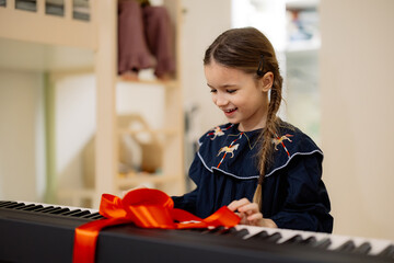 A young girl excitedly opens a gift-wrapped electronic keyboard with a red ribbon.