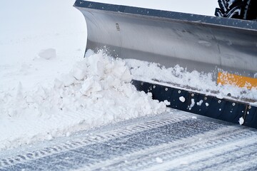 Snowplow blade pushing fresh winter snow off a paved surface, leaving distinct tire tracks