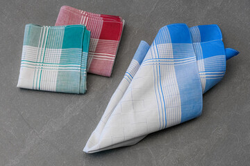 Set of three handkerchiefs in various colors (blue, green, and red) with grey centers and a plaid pattern, photographed on a solid gray surface.