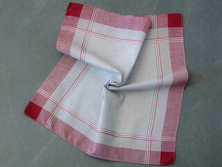 Single red and grey handkerchief, unfolded and slightly rumpled, displaying its plaid border pattern against a gray background.