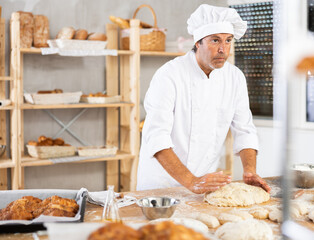 Caucasian guy works in bakery as baker, kneads dough, works with flour. Working moment, process of creating croissants in bakery
