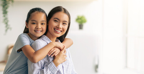 Tenderness and motherhood concept. Cute asian girl hugging young mother from the back, sitting on dinner table at kitchen interior. Mom and her child spending time together at home