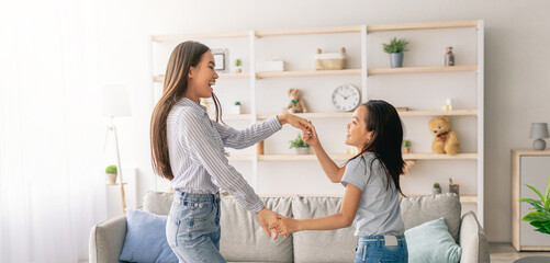 Joyful asian mom and daughter dancing to music, holding hands and enjoying favorite song together,...
