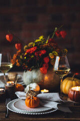 Beautiful elegant table setting for candlelight Thanksgiving Day dinner or Halloween party at home. Fancy dishware, porcelain plates. Floral centrepiece, pumpkins and burning candles as decor