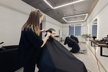 Professional woman barber wielding electric hair clipper making Fashionable haircut. Bearded Man client visit gentleman grooming beauty salon for hairstyle care. Modern Haircut style in barber shop