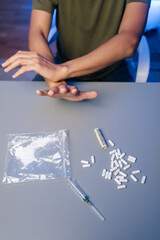 Vertical cropped shot of unrecognizable recovering drug user pushing away narcotics, surrounded by scattered medical tools and paraphernalia, representing personal battle against substance dependency.