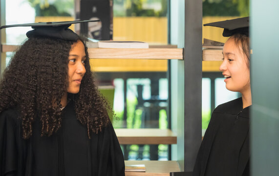 Kids children girl student two person group together smile cheerful happy fun enjoy with frienship graduate cap and gown success education congratulation in library for school college academy campus