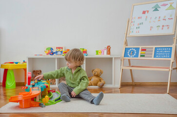 Sweet happy child boy having fun playing with cars and many colorful toys, on the floor, at home