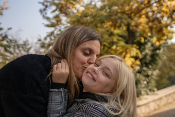 Fototapeta premium Mother daughter kiss. A loving mother kisses her happy daughter on the cheek outdoors in autumn.