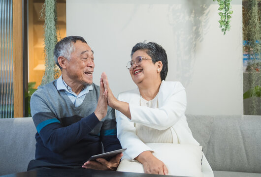 Elderly couple man and woman sit on sofa in cozy living room, use tablet together. appear be engaged in activity on tablet, possibly read browse internet plan your life, business or health insurance. - Powered by Adobe