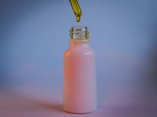 A drop of golden liquid falling from a dropper into a white glass bottle, set against a soft pastel background, symbolizing organic skincare products, wellness, and natural beauty.