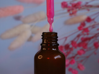 A dropper dispensing vibrant pink liquid into a brown glass bottle, set against a soft pastel background with pink floral accents, symbolizing organic skincare, beauty products, and wellness treatment