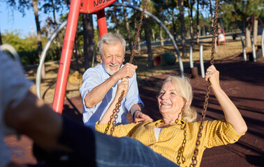 Obraz premium Happy active senior woman having fun on a swing in park outdoors