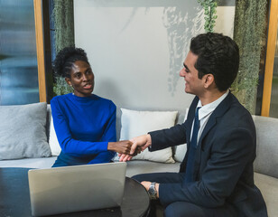 professional business set where two individual  woman and man in dark suit, shaking hand across a white table. there tablet and some document. background office environment with minimalistic decor.