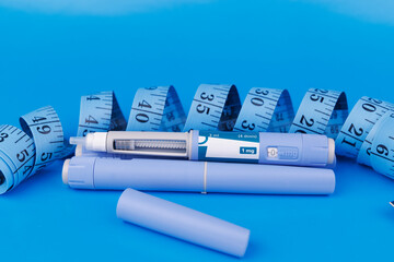 Flat lay composition showing semaglutide pens, red B12 ampoules, pill bottles, and tapes on an...