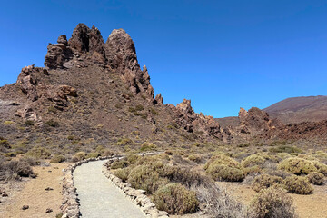 A rocky landscape with a winding path leading through dry vegetation in Roques de Garcia, volcano Teide National Park, Tenerife
