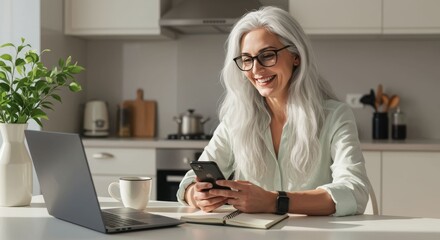 Smiling mature woman with long silver hair using smartphone at kitchen table