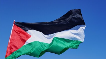 Palestinian flag waving against a clear blue sky, symbolizing solidarity, freedom and human rights while highlighting humanitarian aid, protest and national identity