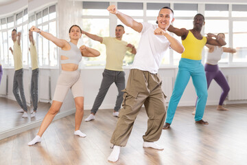 Naklejka premium Young Asian male instructor in casual sportswear enthusiastically guiding diverse class through zumba routine in fitness studio, emphasizing fun and rhythm..