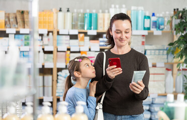 Adult woman with daughter buyers scanning qr code for moisturizing cream in pharmacy