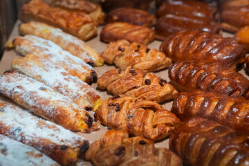 Various golden brown pastries, including puff pastries with powdered sugar and braided buns, arranged on a bakery tray. Suitable for bakery menu design, food advertising, or culinary blog content.
