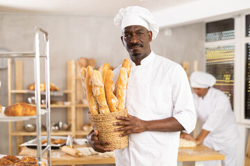 African man baker with basket of baguettes, shows goods. He has made large number of fresh fragrant...
