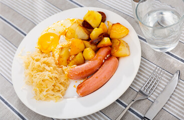 Sausages with fried eggs, potatoes and pickled cabbage served for breakfast