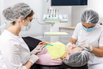 Dentist and assistant performing dental treatment inmodern dental clinic, patient laying in a chair