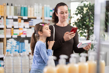 Adult woman with daughter buyers scanning qr code for box of pills in pharmacy