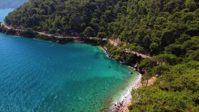 Aerial footage captures the stunning turquoise waters and lush green coastline surrounding the ancient city of Knidos on the Datca Peninsula in Turkey. This serene landscape showcases the natural beau