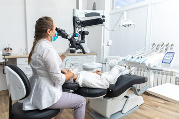 Female dentist using dental microscope treating patient teeth at dental clinic office