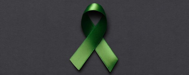 Green awareness ribbon lies on a dark background, representing mental health support