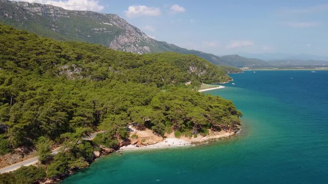 An aerial perspective captures the stunning natural beauty of G&ouml;kova Bay in Turkey, showcasing the vibrant turquoise waters of the Aegean Sea meeting lush green, pine covered cliffs and a serene coast
