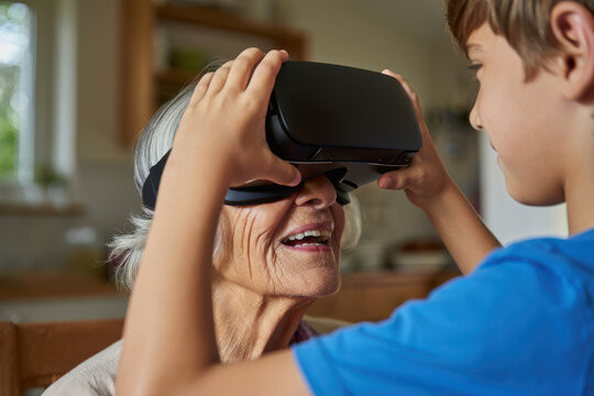 Adorable grandson helps his delighted grandmother try on a VR headset, experiencing modern technology with joy. - Powered by Adobe