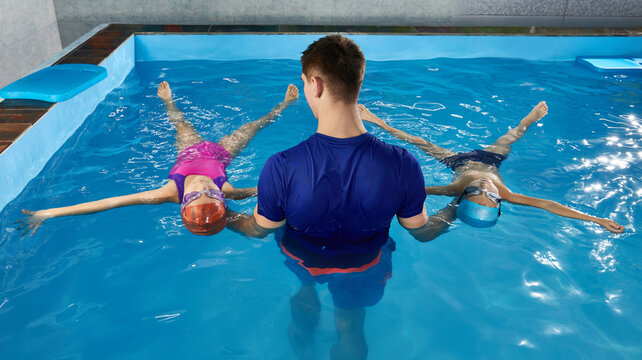 Little children learning how to swim in pool with teacher