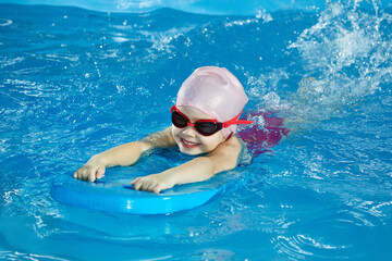 Little girl learning to swim in indoor pool with pool board