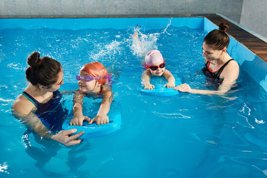 Little girl learning to swim in indoor pool with pool board and trainer - Powered by Adobe