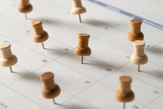 Wooden push pins marking important dates on a calendar, symbolizing planning, scheduling, reminders, and organization.