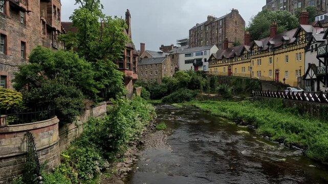 footage video of Dean Village in Edinburgh, Scotland, a picturesque historic riverside settlement along the Water of Leith with stone bridges, medieval buildings, and lush green valley views.