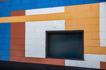A colourful  painted cinder block wall, with a boarded up pass through window, daytime, nobody 