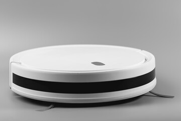 Black and white image of a white robotic vacuum cleaner with a black stripe, resting on a smooth grey surface. A modern solution for smart home cleaning.

