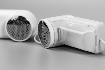 A monochrome close-up of two electric fabric shavers on a grey surface. These modern lint removers are perfect for keeping garments fresh and free of pills.

