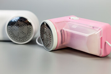 Pink and white electric fabric shavers on a grey surface. The perfect home tool for removing lint and pilling to extend the life and refresh the look of your clothes.

