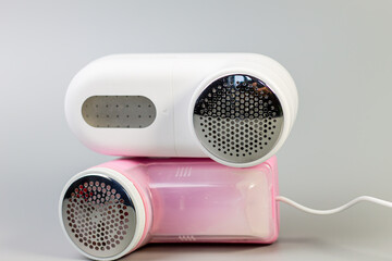 A stylish pair of electric fabric shavers in white and pink, stacked against a neutral grey background. The perfect tools for removing lint and pilling, keeping clothes looking their best.

