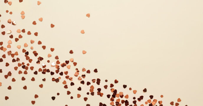 Scattered sparkling rose gold heart confetti creating a festive and romantic background on a light cream surface.