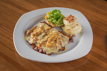 Grilled Steak Topped with Melted Cheese, served with Mashed Potatoes and Guacamole